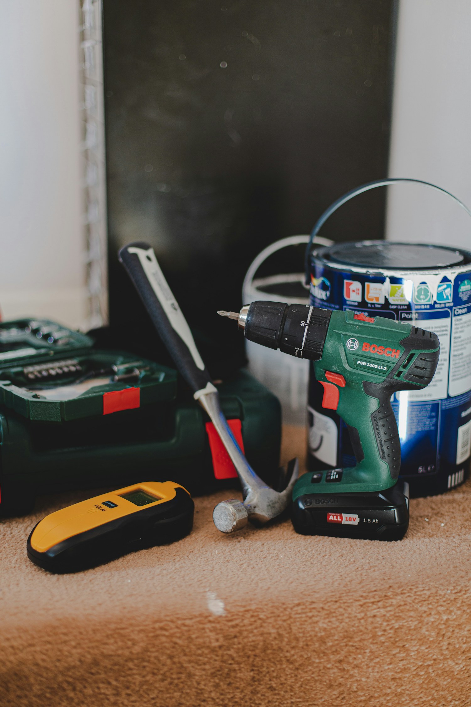 A cordless drill, hammer, and stud finder arranged for a home project